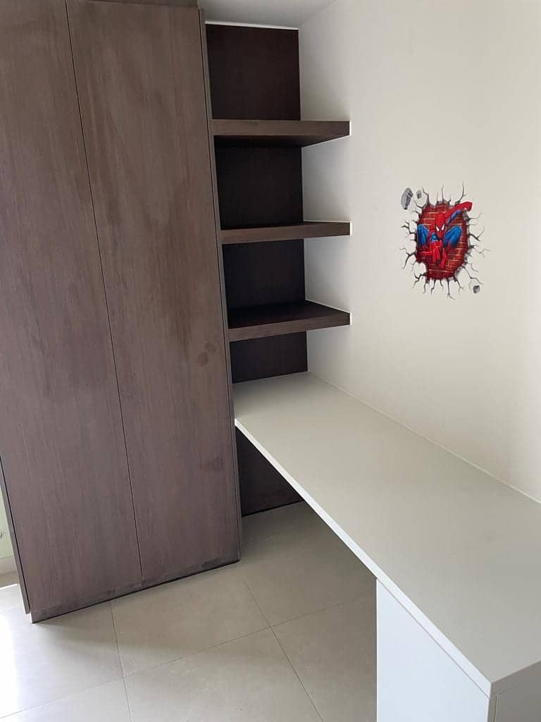 Hoge donkere kast naast zwevende legplanken en een wit bureau