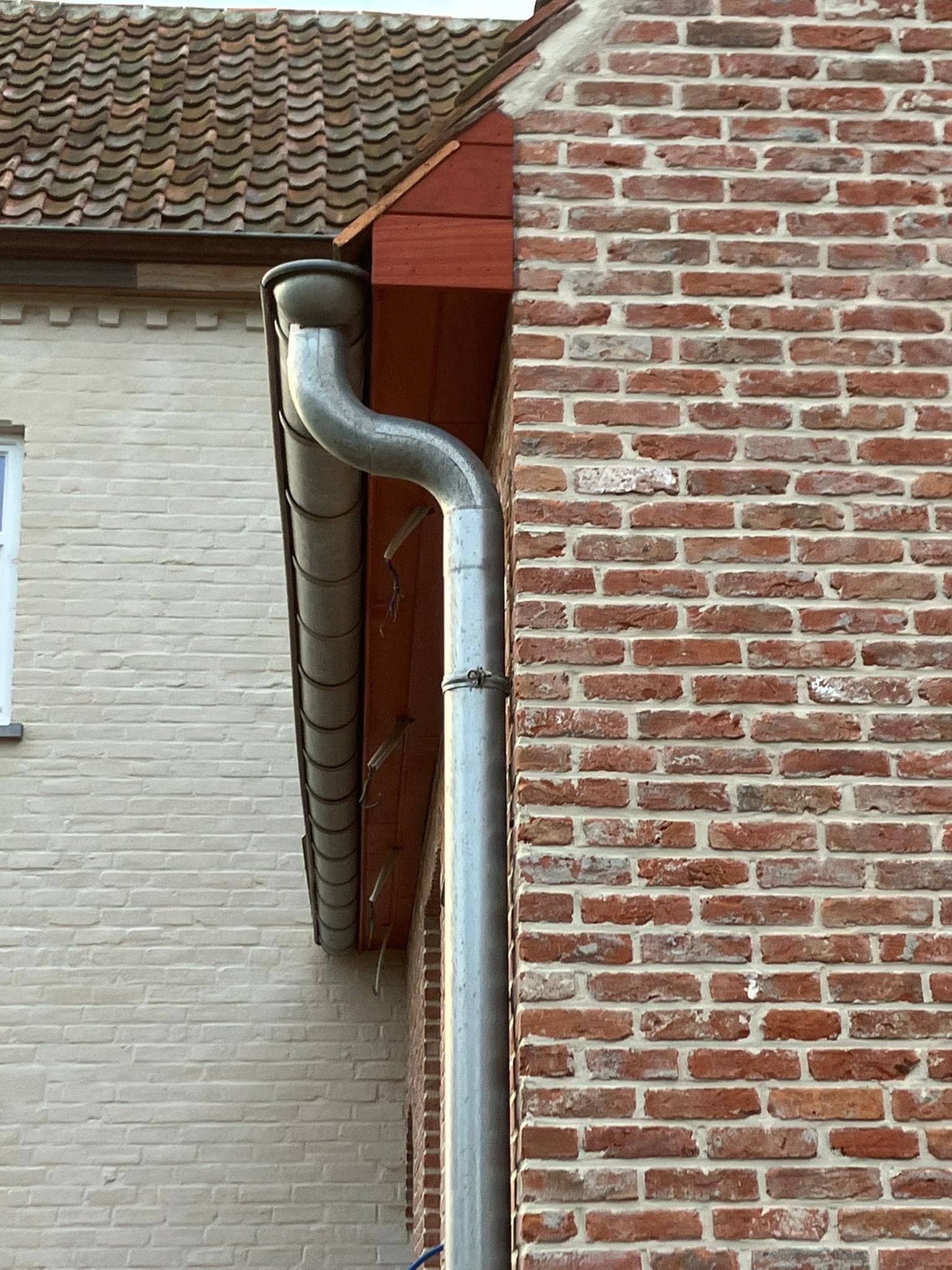 Zinken regenpijp langs een houten bakgoot