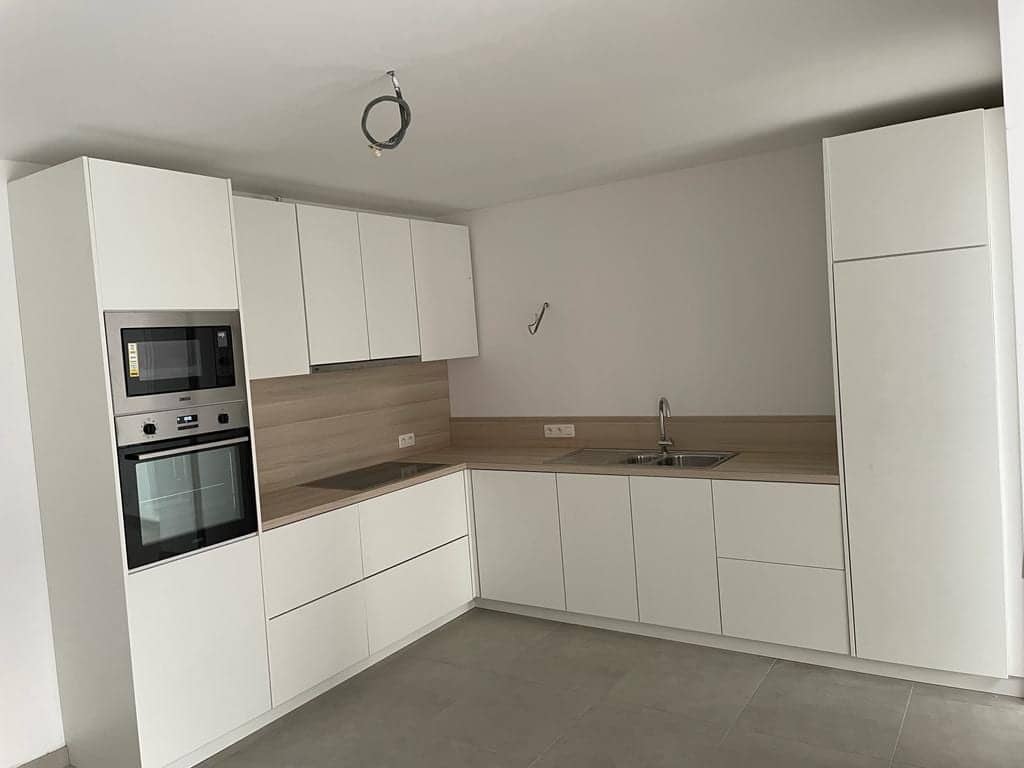 Witte hoekkeuken met houten werkblad en een hoge kolom met oven en microgolfoven