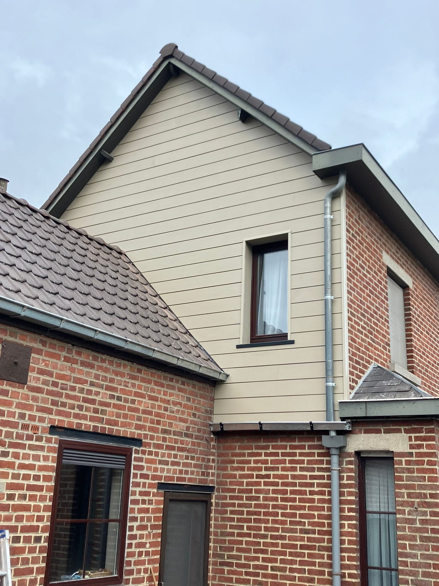 Afgewerkte gevel met lichte Cedral planken boven een bakstenen woning