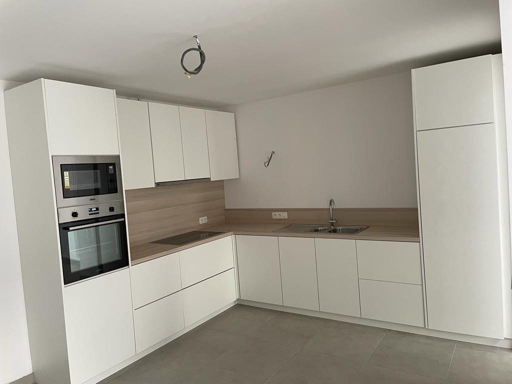 Witte hoekkeuken met houten werkblad en een hoge kolom met oven en microgolfoven